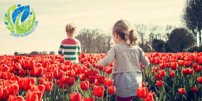 Two girls walking through flowers with Essential Bracelet logo in the corner